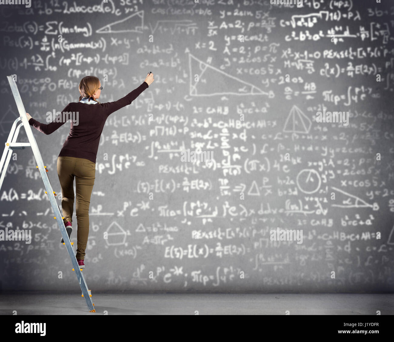 Studentin steht auf einer Leiter und schreibt Mathematik Formeln Stockfoto