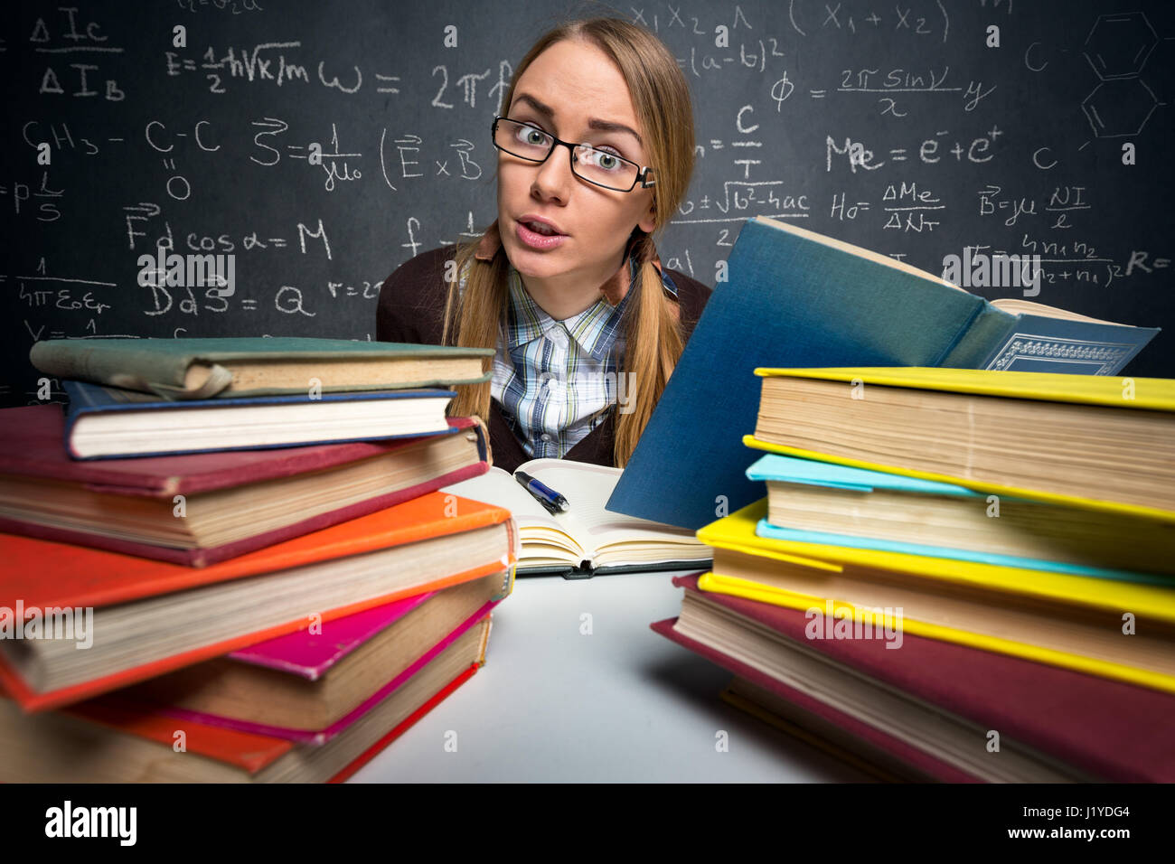 Studenten sitzen an einem Schreibtisch voller Bücher, schockiert Ausdruck Stockfoto