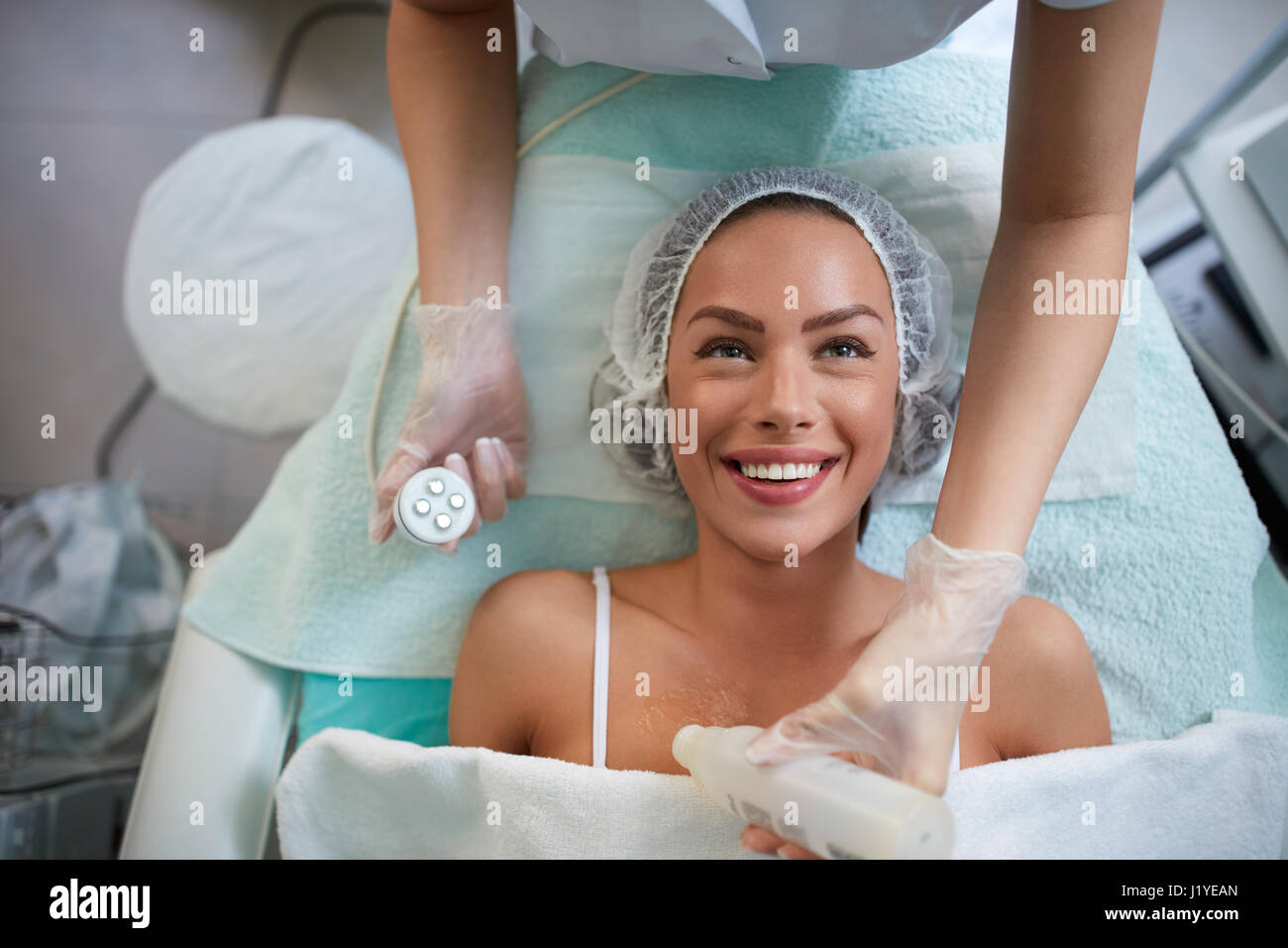 Fröhliches Mädchen empfängt Gesichtsbehandlung von Kosmetikerin, Dame liegen und 4D Laser lifting Gesicht lächelnd Stockfoto