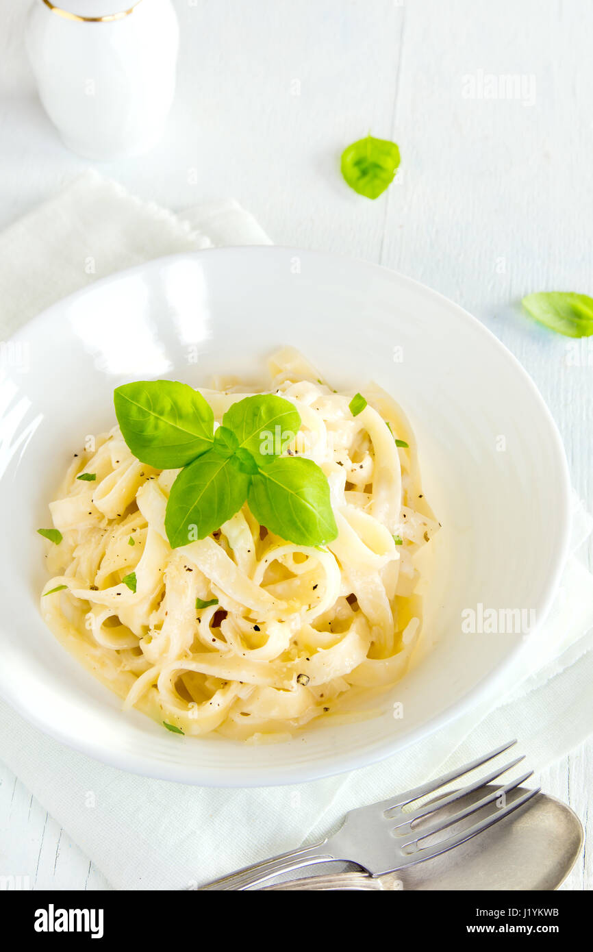 Alfredo-Tagliatelle-Nudeln mit Basilikum und schwarzem Pfeffer in weiße Schüssel - hausgemachte cremige Pasta mit Alfredo Soße Stockfoto