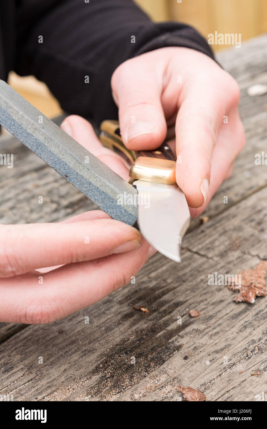 Männliche Hände mit einem Schleifstein schärfen große Taschenmesser. Stockfoto