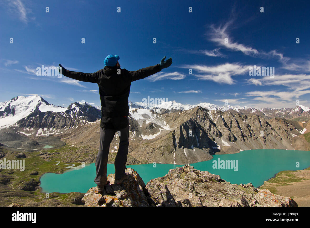 Mann in schwarzer Jacke Stand mit Hände hoch über dem blauen ruhigen Berg See Alakol mit Bergen umgeben Stockfoto