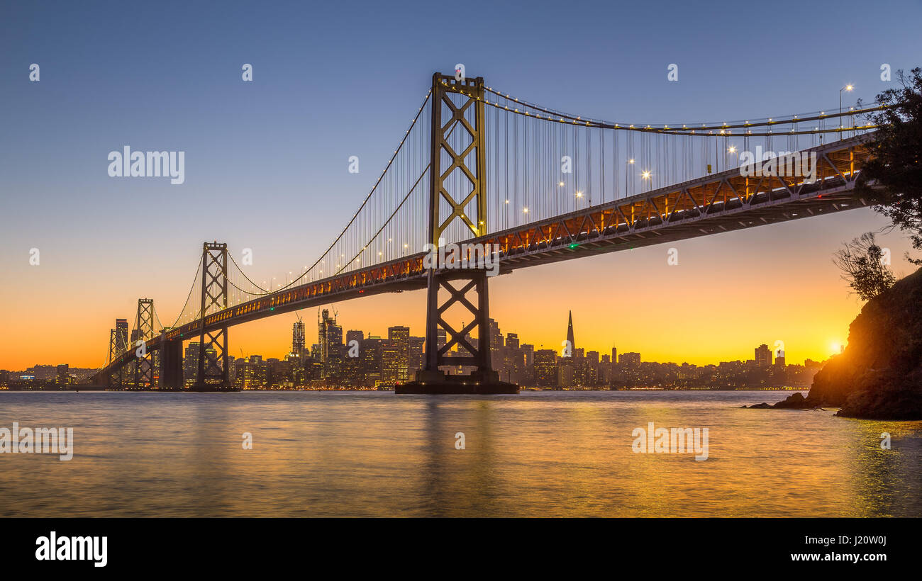 Klassische Panoramablick auf die Skyline von San Francisco mit berühmten Oakland Bay Bridge beleuchtet im schönen goldenen Abendlicht bei Sonnenuntergang im Sommer, San Stockfoto