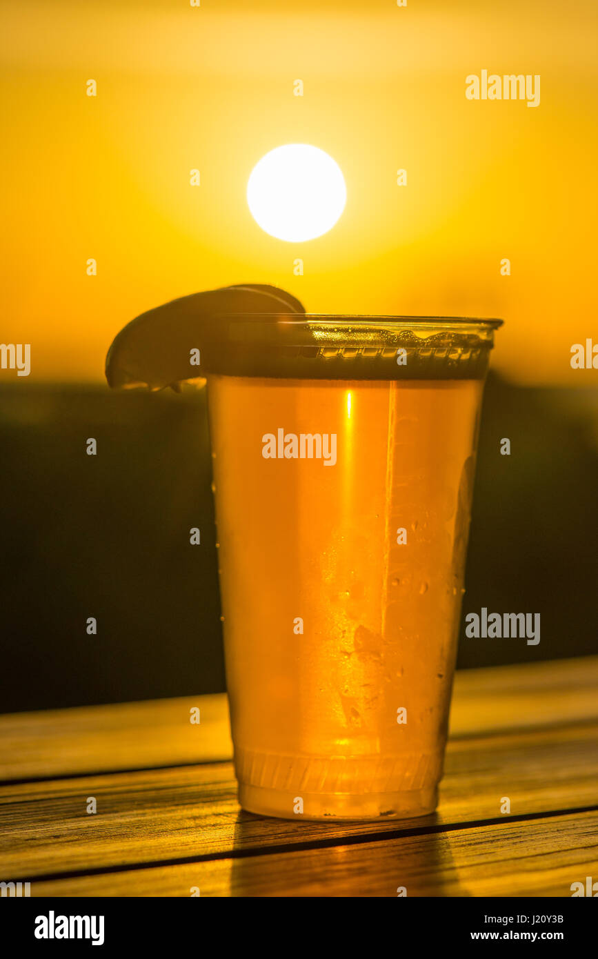 Eiskaltes Bier mit einem Kalk-Keil, wenn die Sonne im Hintergrund am Strand untergeht Stockfoto