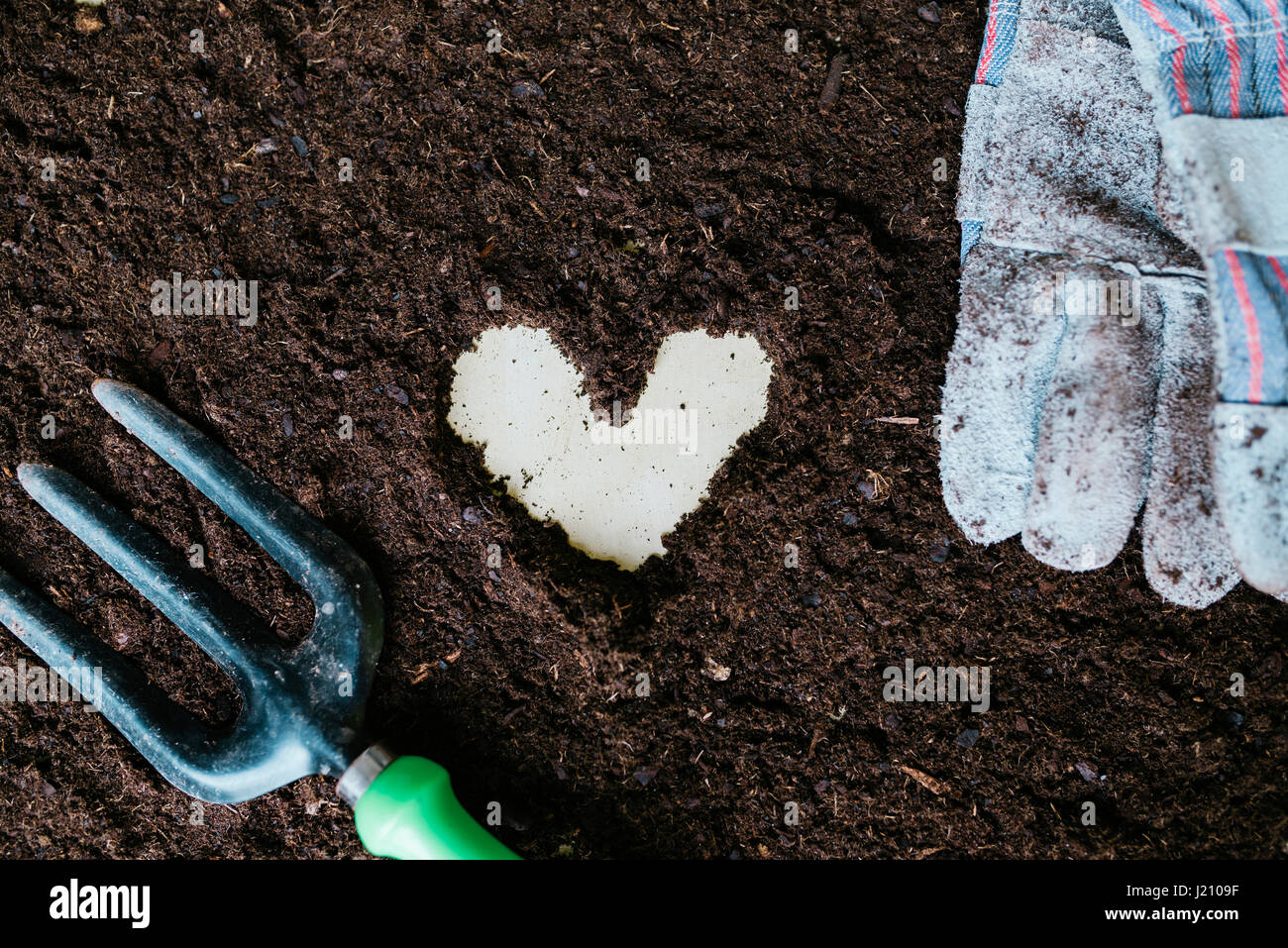 Herzform mit Gartenerde, Gartenwerkzeug und Handschuhe gemacht Stockfoto