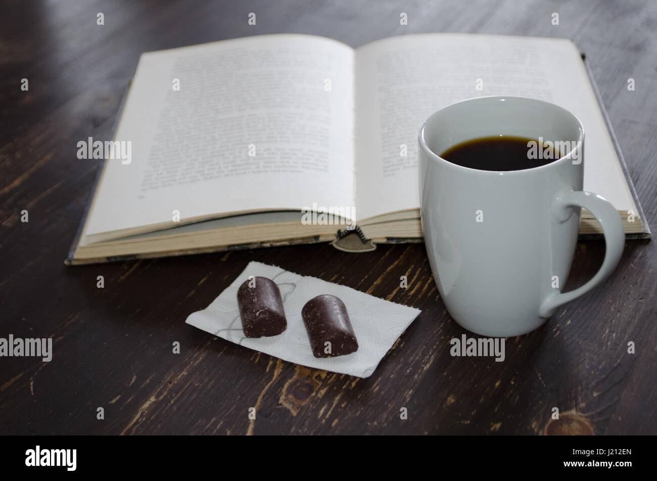 Tasse Kaffee und zwei kleine Pralinen Inn Vorderseite des Buches auf braunen Holztisch Stockfoto