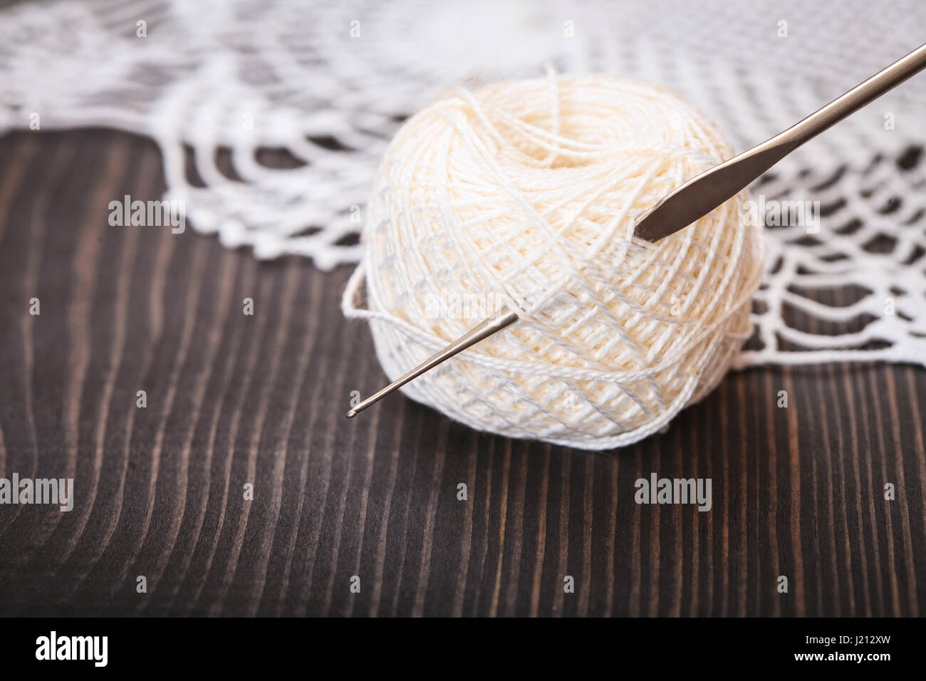 Strang aus weißen Garn und Häkelnadel auf einem Holztisch Nahaufnahme Stockfoto