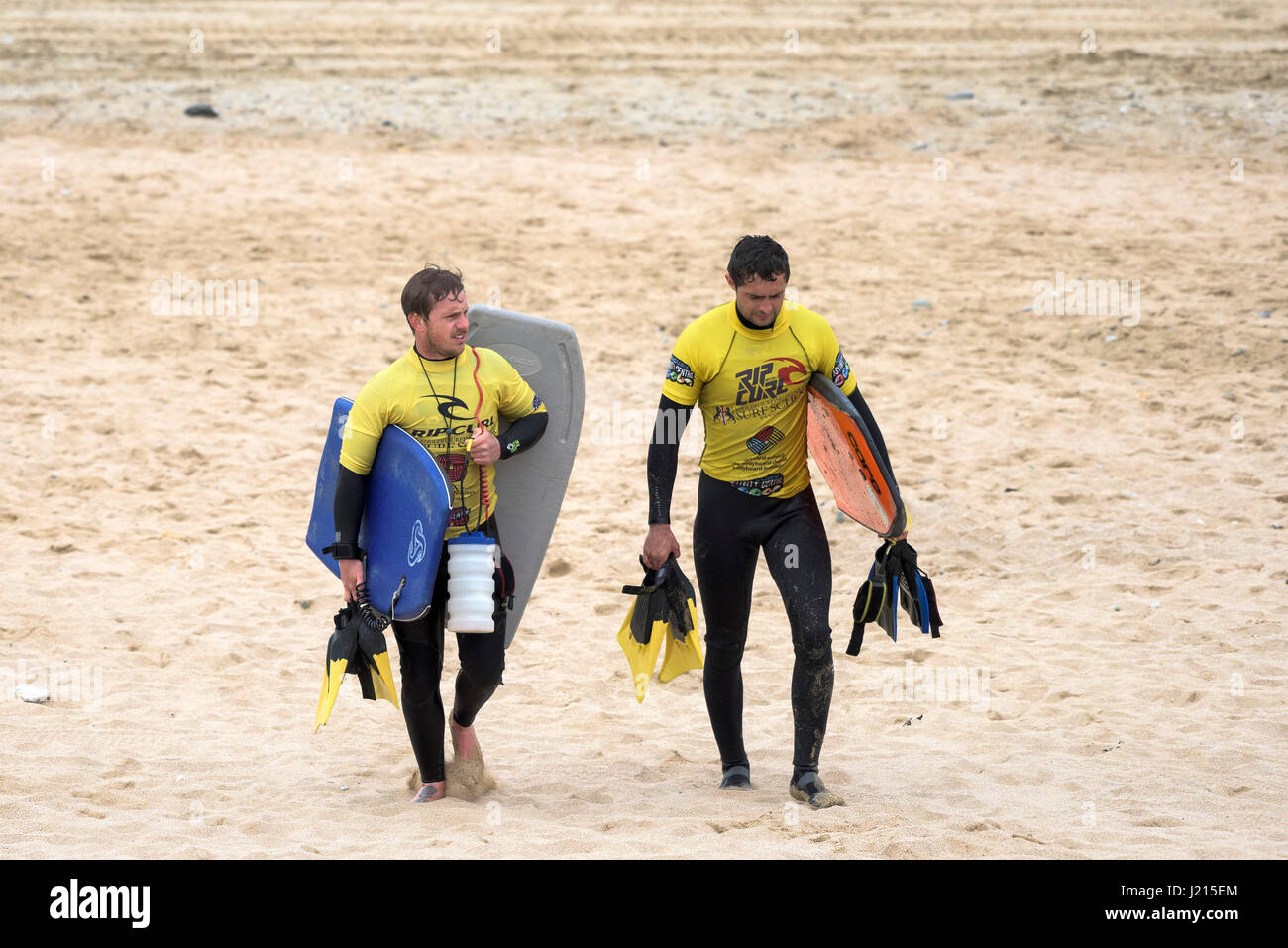 Zwei Instruktoren zu Fuß über den Strand Bodyboards Surf Schule Sand Freizeitbeschäftigung Fistral Cornwall UK Stockfoto