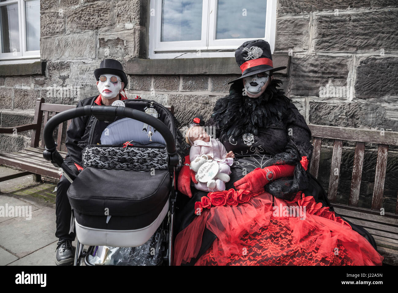 Männlichen und weiblichen Goth sitzen auf Bänken am Meer am Whitby Gothic Weekend und sie wiegen eine lebensechte Babypuppe Stockfoto