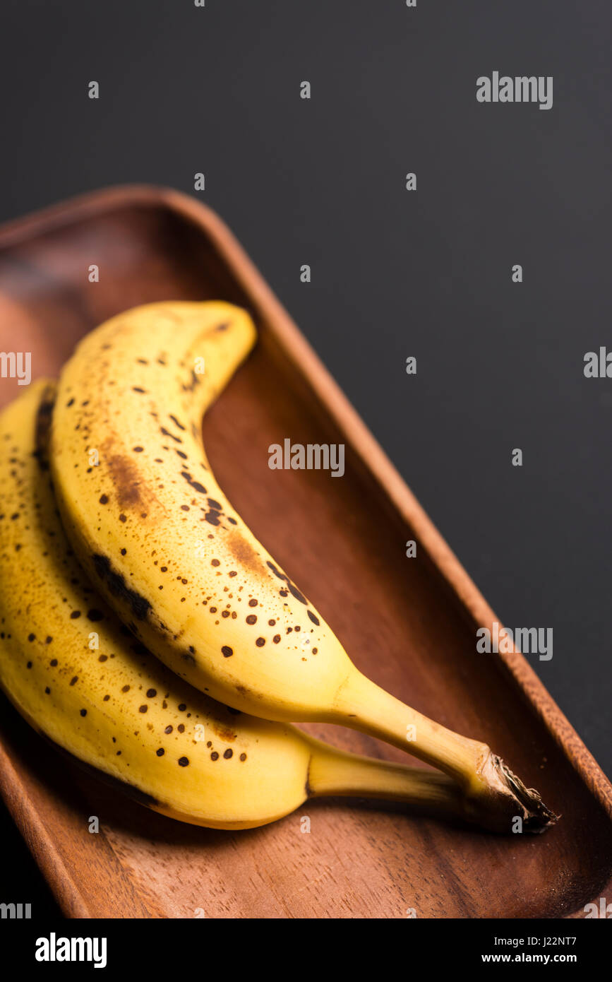 Zwei Bio-Bananen in einem Holz über ein schwarzes Brett. Stockfoto