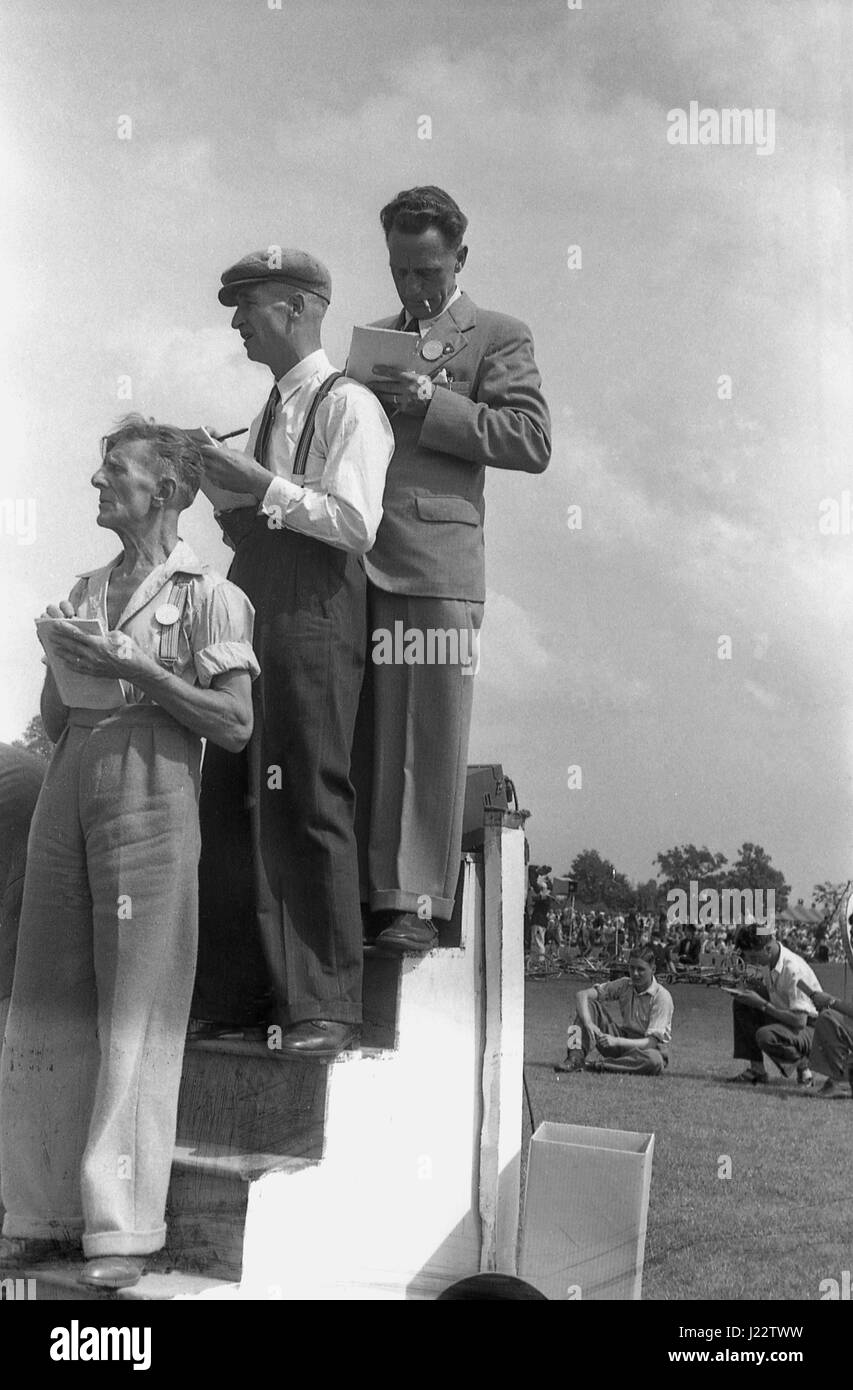 1950er-Jahren, historische, machen drei männliche Zeitmesser auf einem erhöhten hölzernen Zeitmessung Stand Notizen, wie sie die Finisher auf eine outdoor Amateur Leichtathletik meeting überprüfen, England, UK. Stockfoto