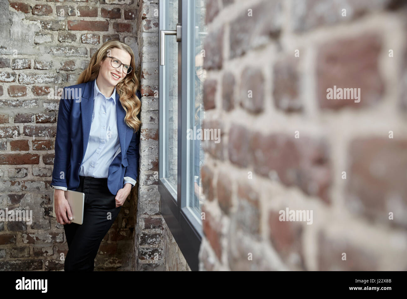 Lächelnde Geschäftsfrau gelehnt Ziegelwand mit tablet Stockfoto