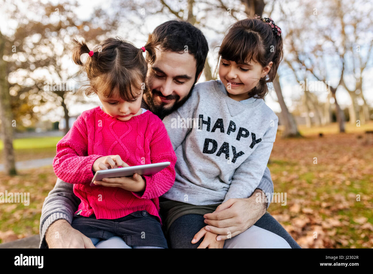 Vater mit seinen kleinen Töchtern Blick auf Tablet im herbstlichen park Stockfoto