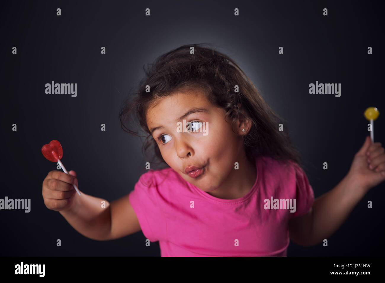 Kleines Mädchen in rosa T-shirt hält zwei Lutscher mit Gesichtsausdruck. Stockfoto