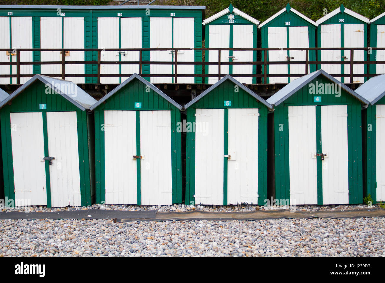 Gleichmäßigen Reihen von traditionellen, grün und weiß lackiert Strandhütten an einem britischen Strand mit Schlösser an den Türen. Stockfoto