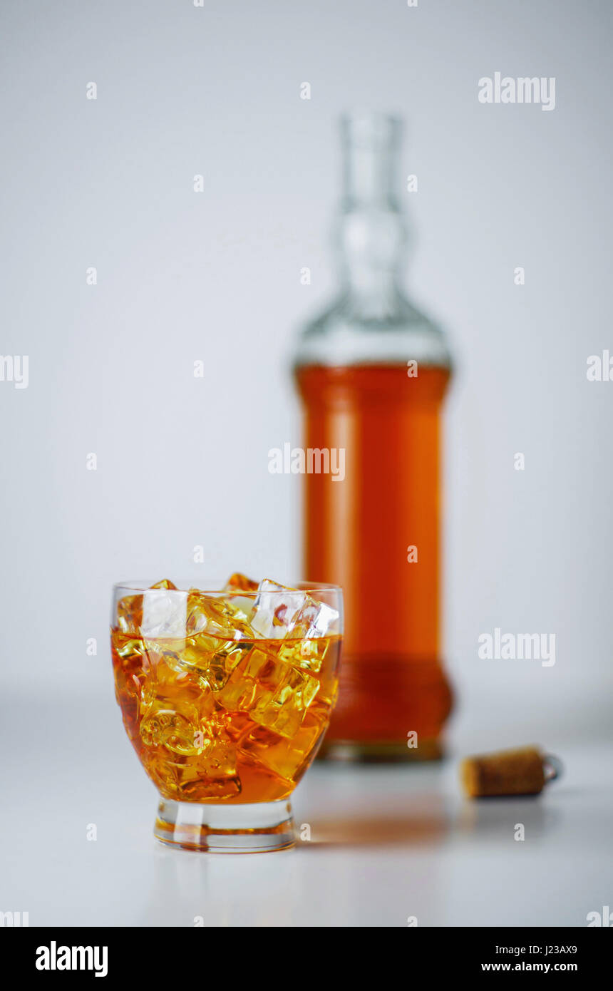 Glas voll Eiswürfel und alkoholisches Getränk und eine Flasche im Hintergrund Stockfoto
