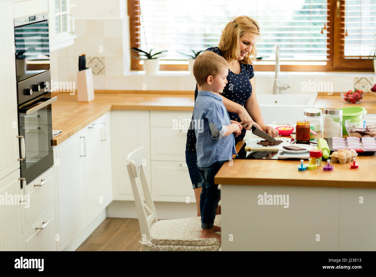 Intelligente nettes Kind, die Mutter in der Küche und bereitet Cookies helfen Stockfoto