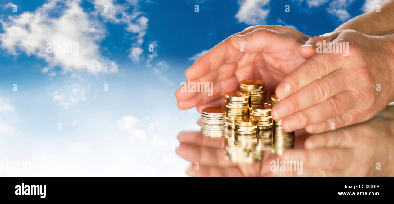 Hände umfassen mehrere Stapel Münzen vor blauem Himmel. Stockfoto