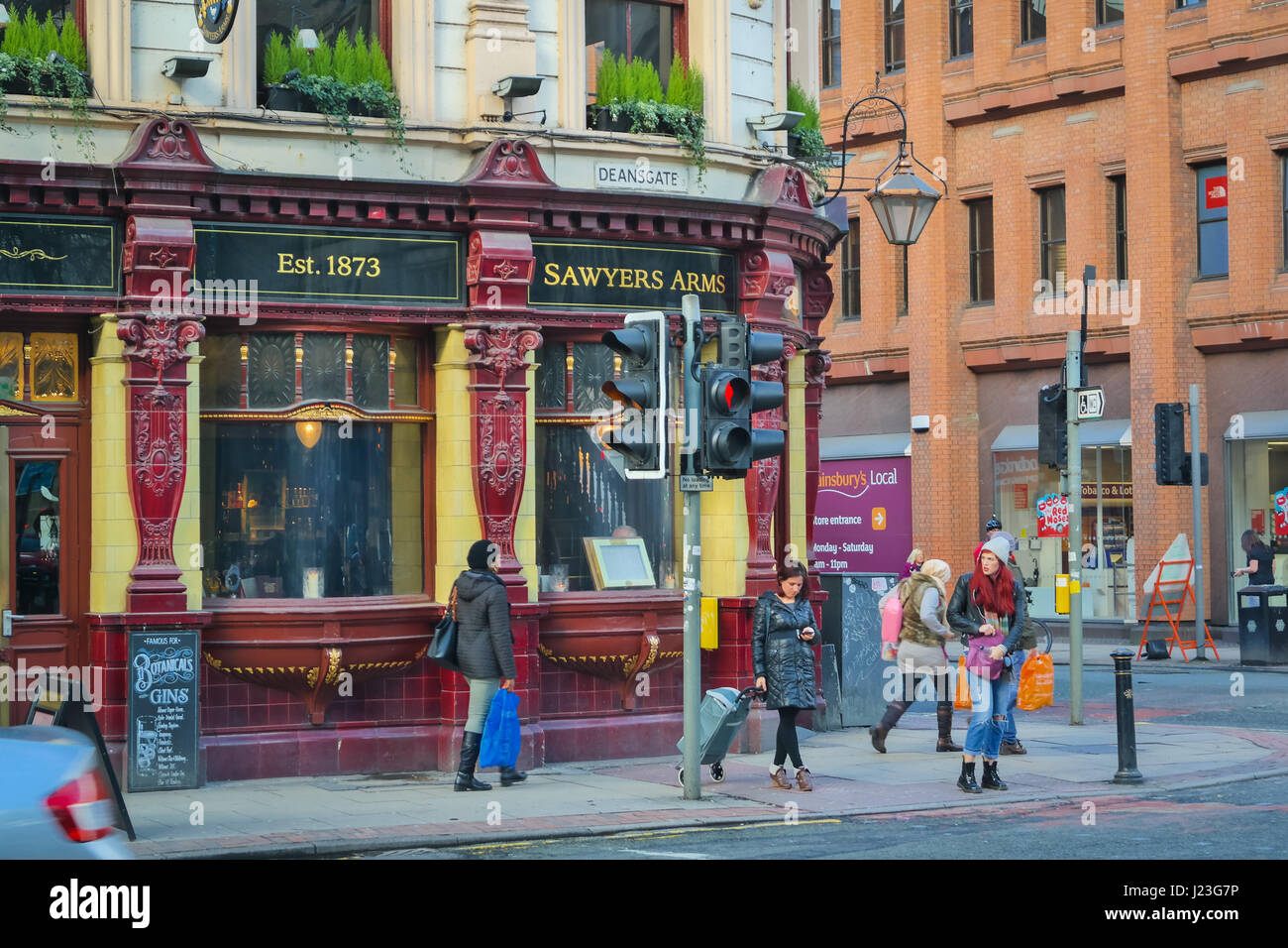 Straße mit der historischen Säger Arms Pub und Frau mit roten Haaren, die die Straße überqueren, Manchester, UK Stockfoto