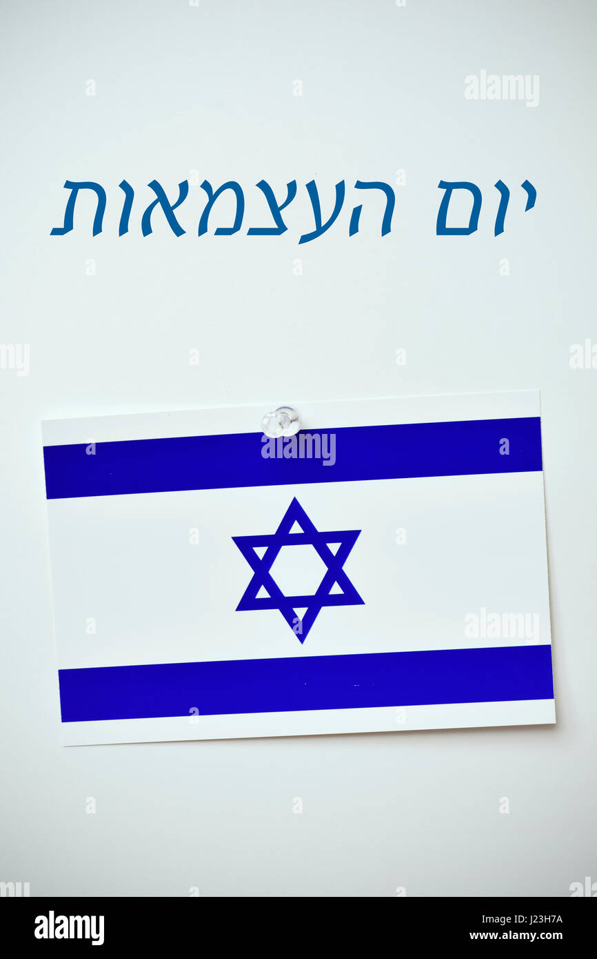 der Text Tag Israels in Hebräisch geschrieben und eine israelische Flagge mit einer Stecknadel zu einem Off-White Hintergrund merken Stockfoto