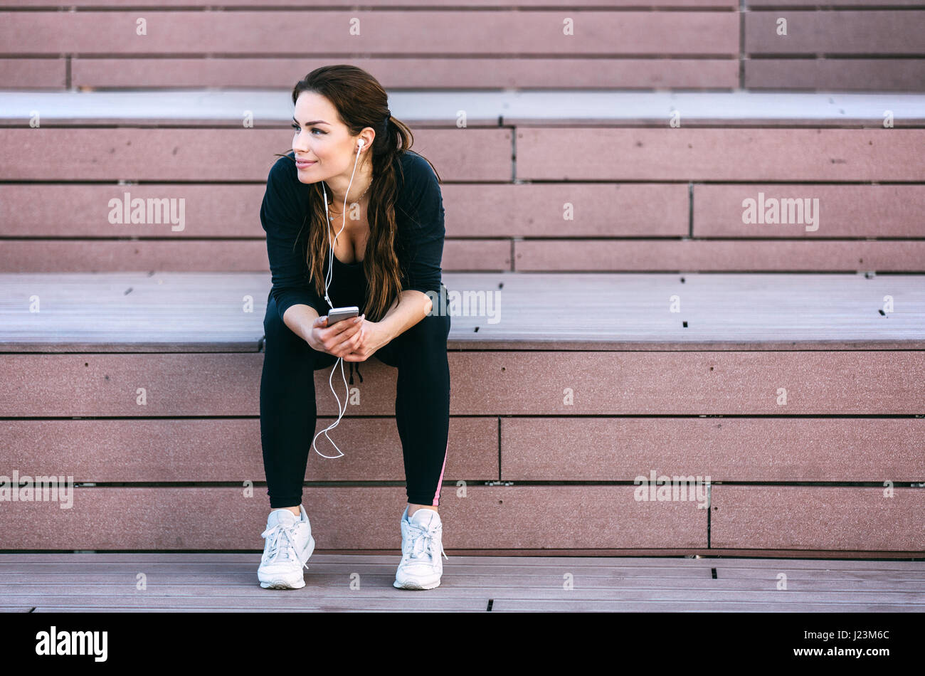 Junge schöne Lächeln passt Frau mit Smartphone beim stillstehen auf großen Treppen. Stockfoto