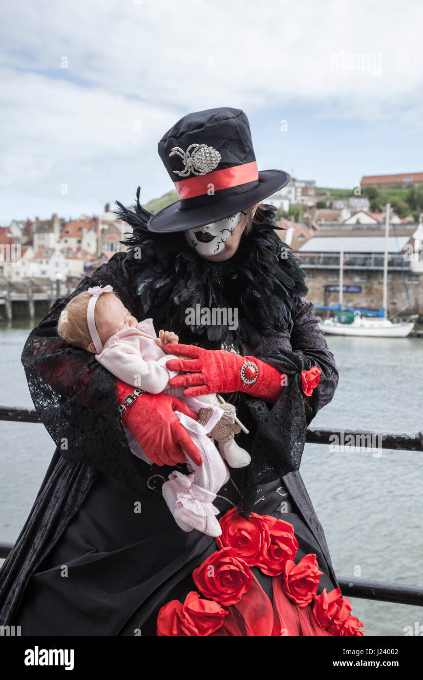 Eine weibliche Goth Stand wiegt eine lebensechte Babypuppe bei Whitby Strand von den halbjährlichen Goth Wochenende feiern Stockfoto