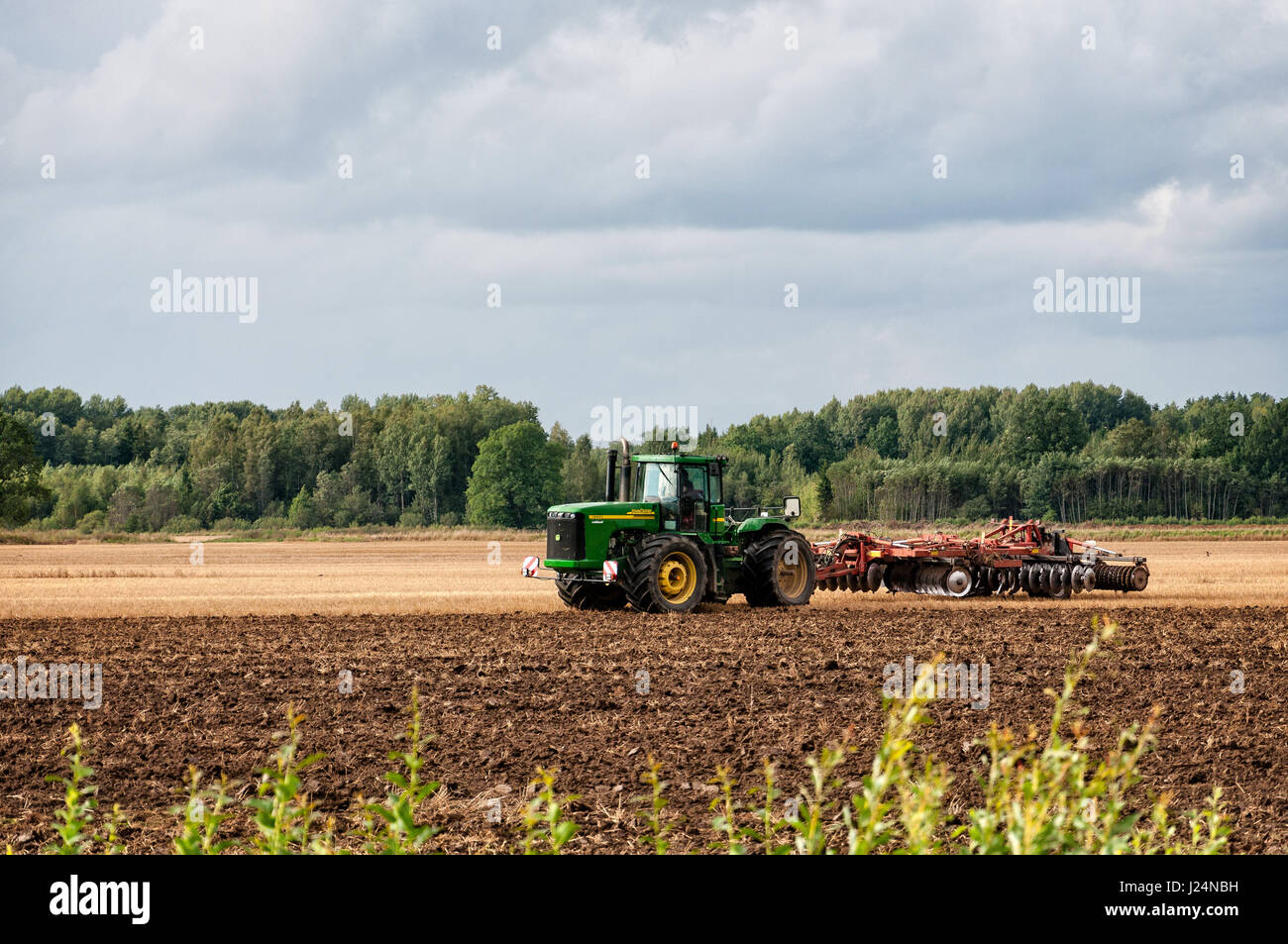 DOBELE, Lettland - 9. August 2011: Grüne Traktor den Boden für die neue Ernte verarbeitet. Stockfoto