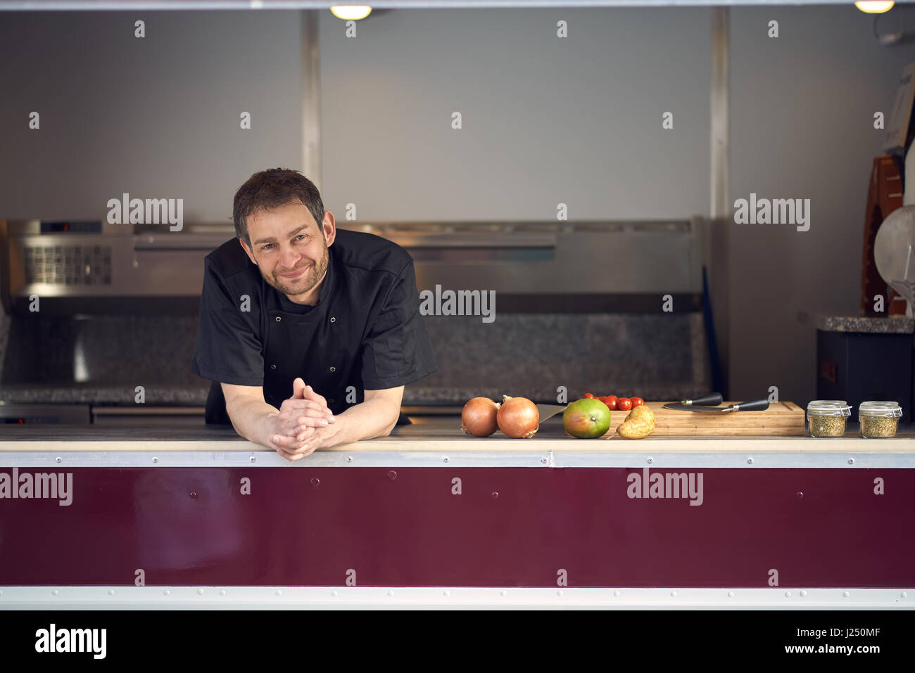 Lächelnd männlichen Chef in Küche stützte sich auf Zähler mit Zutaten kochen Stockfoto