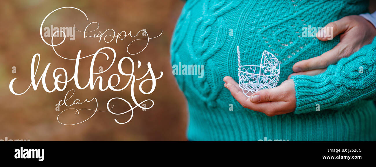 Schwangerschaft-Konzept: Bauch mit Hand kleines Spielzeug Kinderwagen vor und Text Happy Muttertag. Kalligraphie-Schriftzug Hand zeichnen Stockfoto