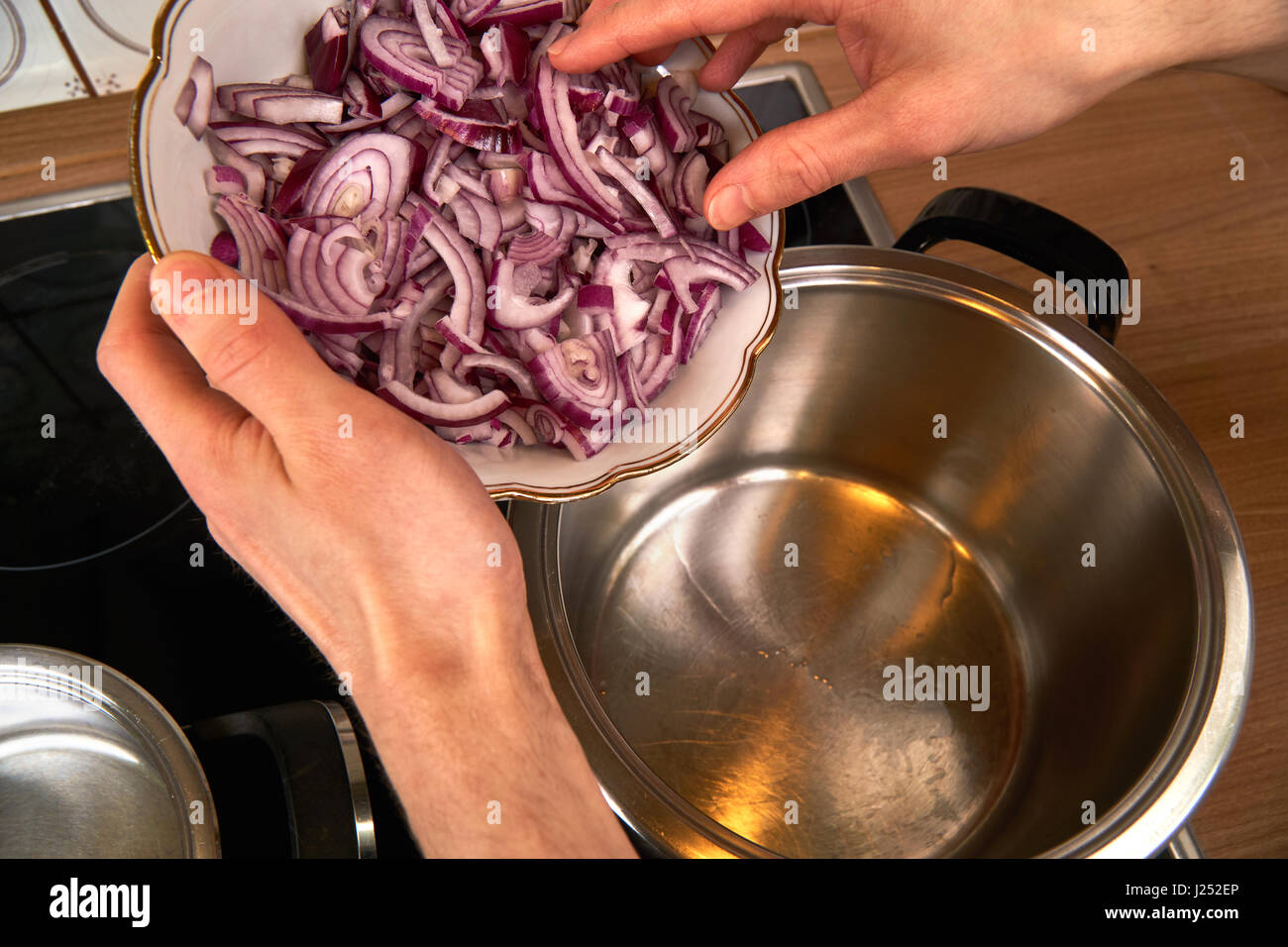 Blick auf Händen eines Mannes Braten Zwiebeln in einem Topf mit Kokosnuss-Öl. Stockfoto