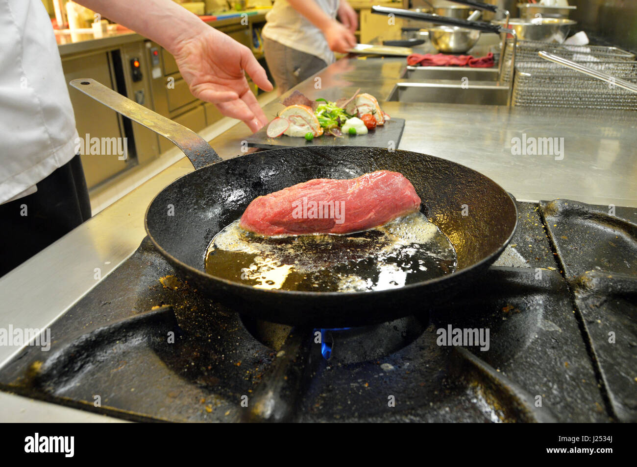 Professioneller Koch backt ein Steak in der Pfanne Stockfoto