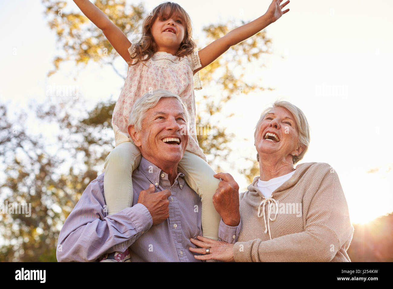 Großeltern geben Enkelin A Schulter fahren im Park Stockfoto