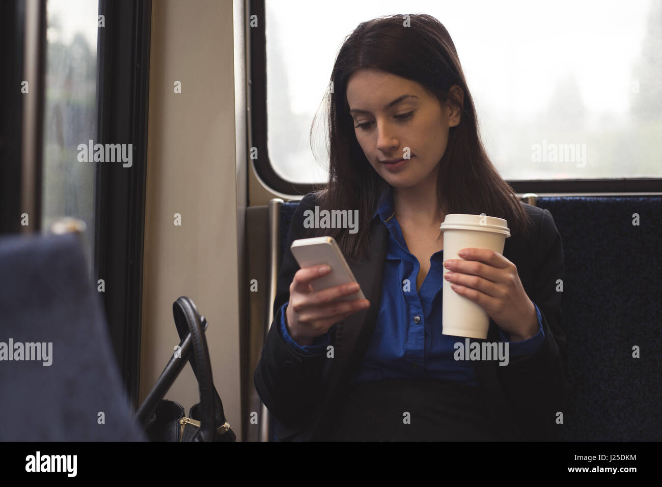 Frau mit Handy und halten Kaffee Tasse beim Sitzen im Zug Stockfoto