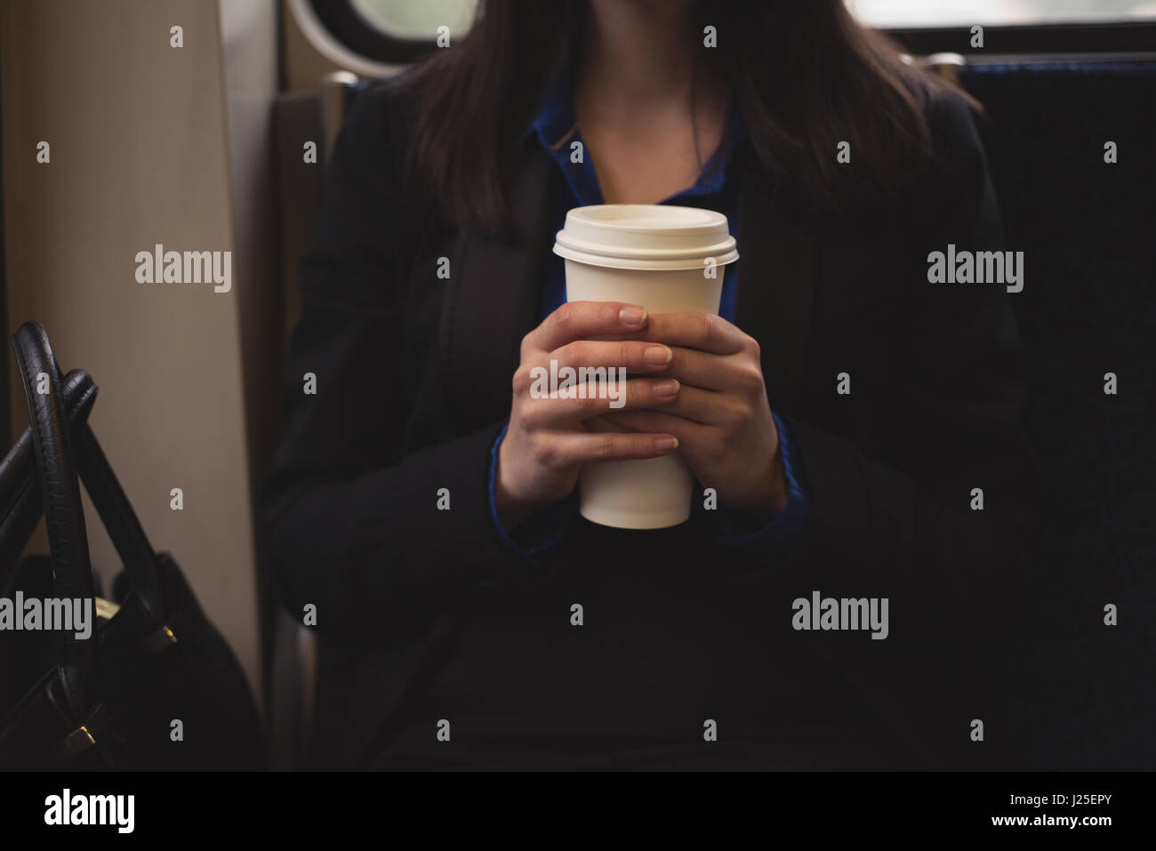 Mittelteil der Frau, die Tasse beim Sitzen im Zug Stockfoto