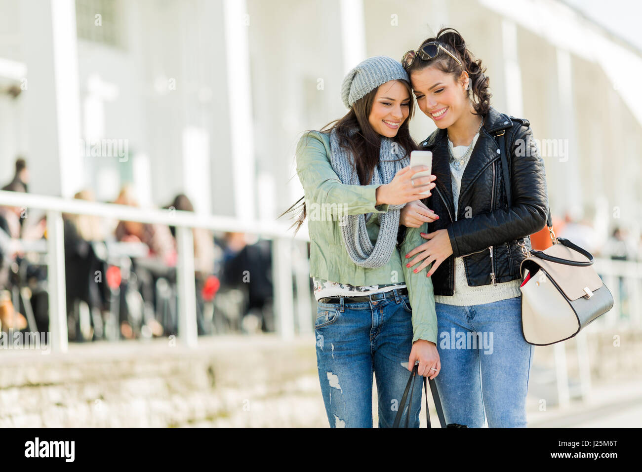 Zwei junge, schöne Frauen betrachten das Telefon während in der Nähe von jeden anderen Stockfoto