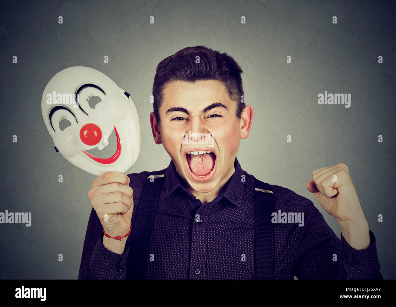 Porträt verärgert böse schreienden Mann Clownsmaske mit dem Ausdruck ihrer Fröhlichkeit Glück auf graue Wand Hintergrund isoliert halten. Menschliche Emotionen Gefühle Stockfoto