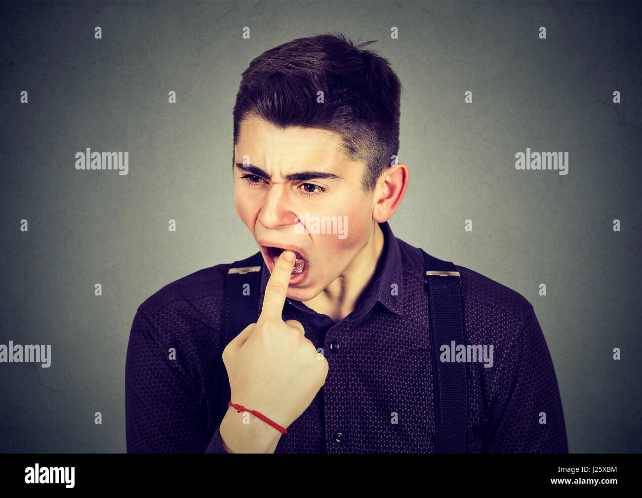 angewidert Mann mit Finger im Mund unzufrieden will kotzen auf graue Wand Hintergrund isoliert. Menschliche Emotionen Körpersprache Stockfoto