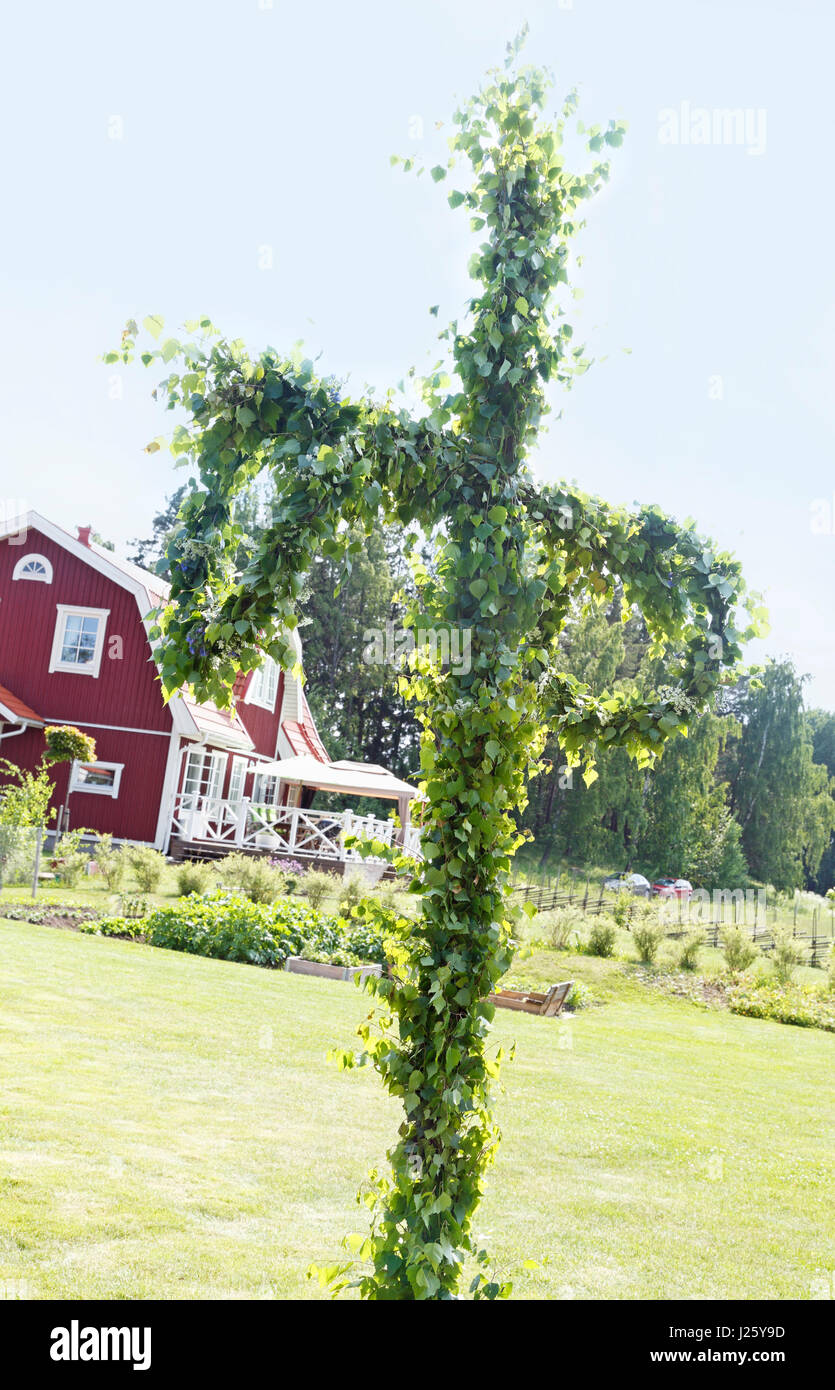Schwedische Mittsommer Pol Baum Birkenzweigen und Blumen. Schweden. Rotes Haus mit weißen Ecken im Hintergrund. Stockfoto