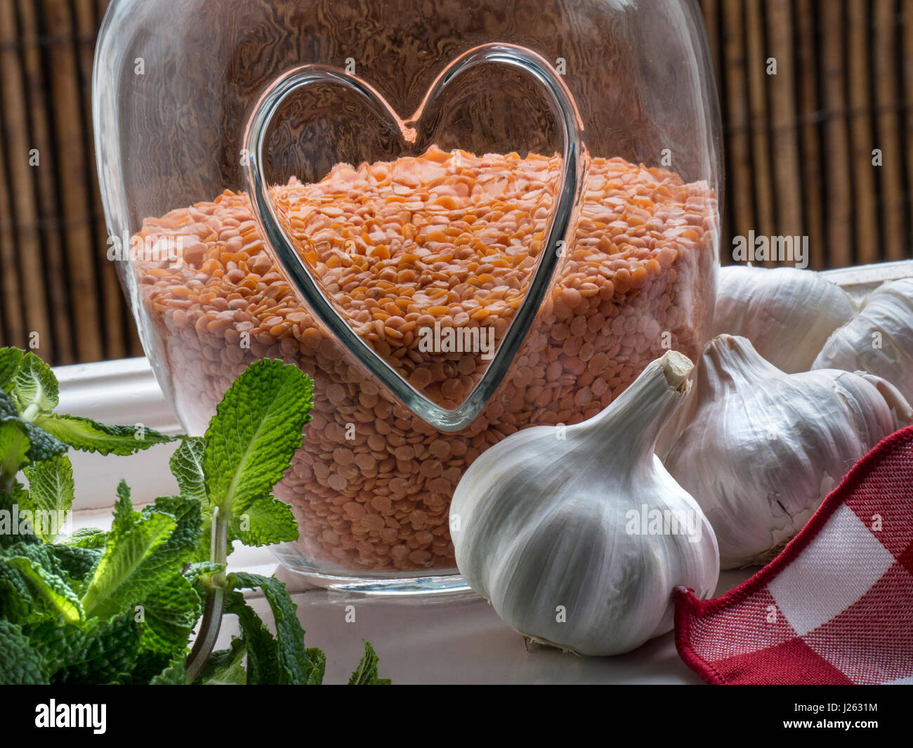 Gesund Essen & Glas mit Herz Motiv mit roten Linsen, eine gesunde genießbare Puls Leguminosen, mit Knoblauch und Zweig Minze durch offene Küche Fenster Stockfoto