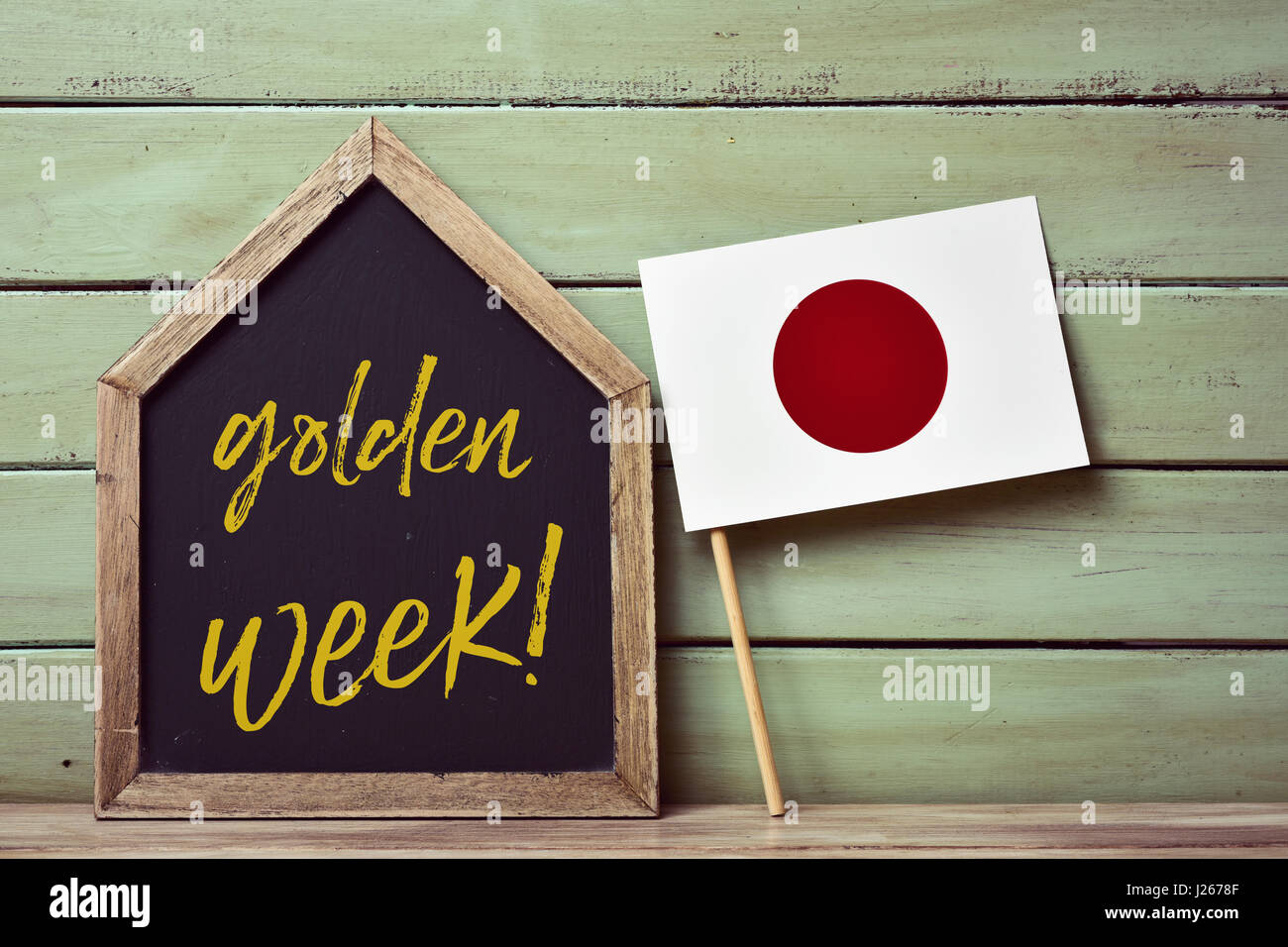 eine Haus-förmigen Tafel mit dem Text Goldene Woche geschrieben und eine Fahne von Japan, gegen einem blassen Grün rustikalen hölzernen Hintergrund Stockfoto