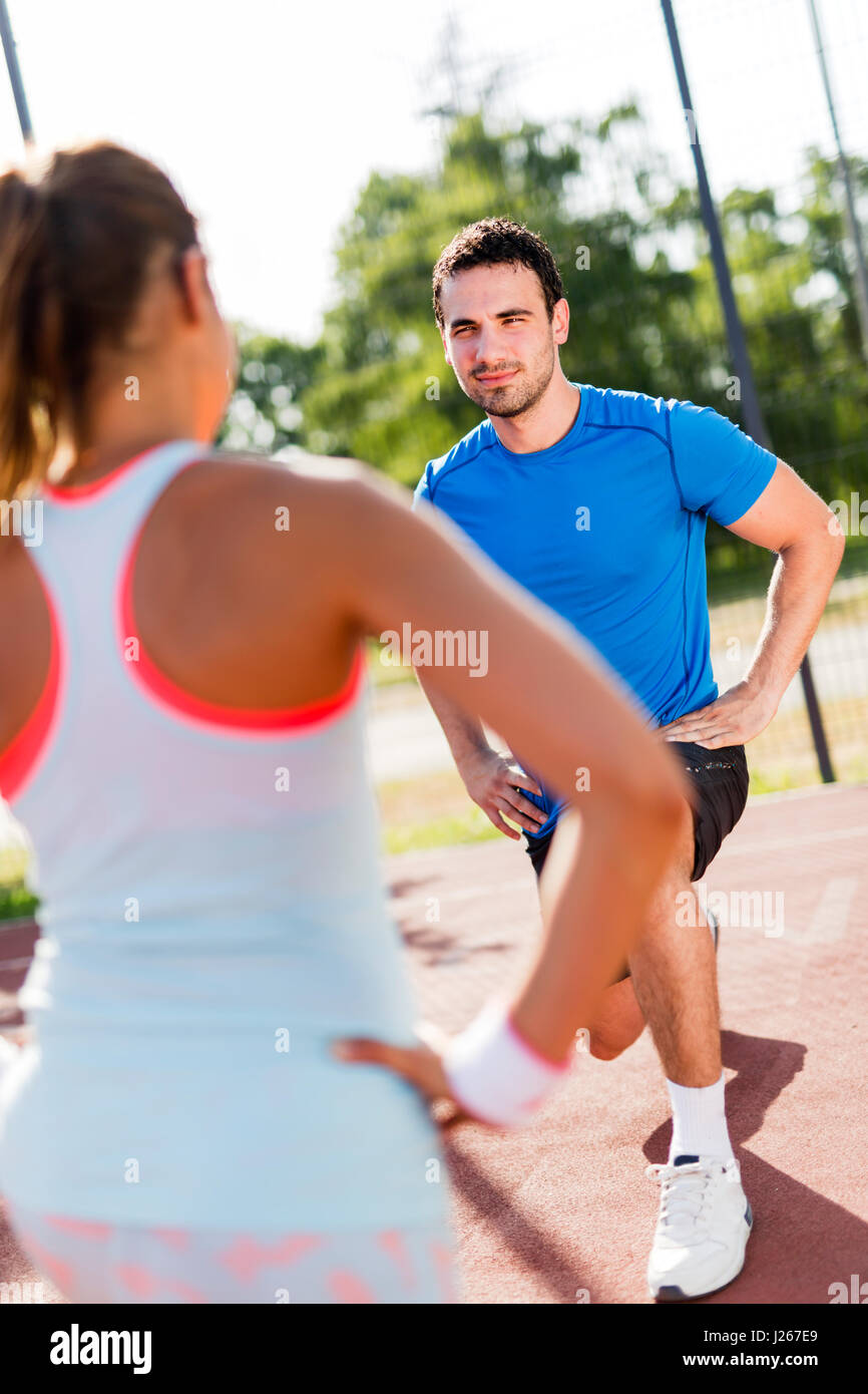Junger sportlicher Mann und Frau dehnen im Freien an einem heißen Sommertag einander zugewandt Stockfoto