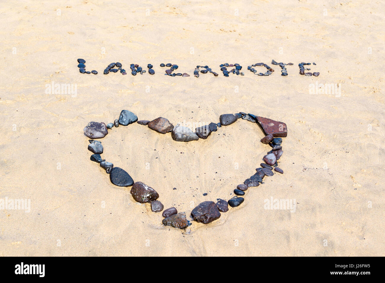 Wort-Lanzarote und ein Herz mit schwarzen Steinen auf einem goldenen Sandstrand geschrieben Stockfoto