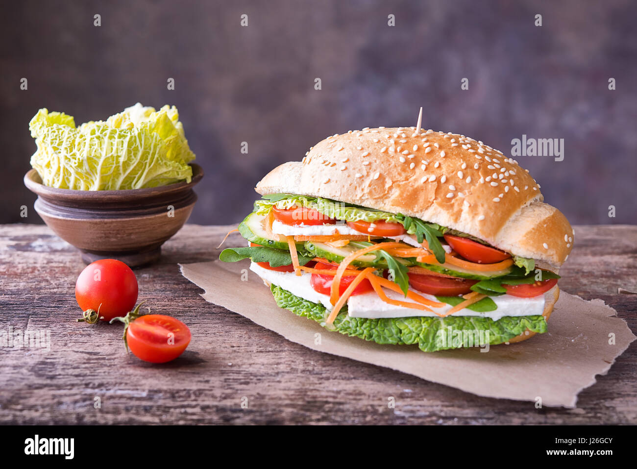 Leckere bunte Sandwich weiß-Brot mit Sesam, Karotte, Gurke, weißer Käse, Kraut und Rucola Salat auf ein Stück Packpapier Stockfoto