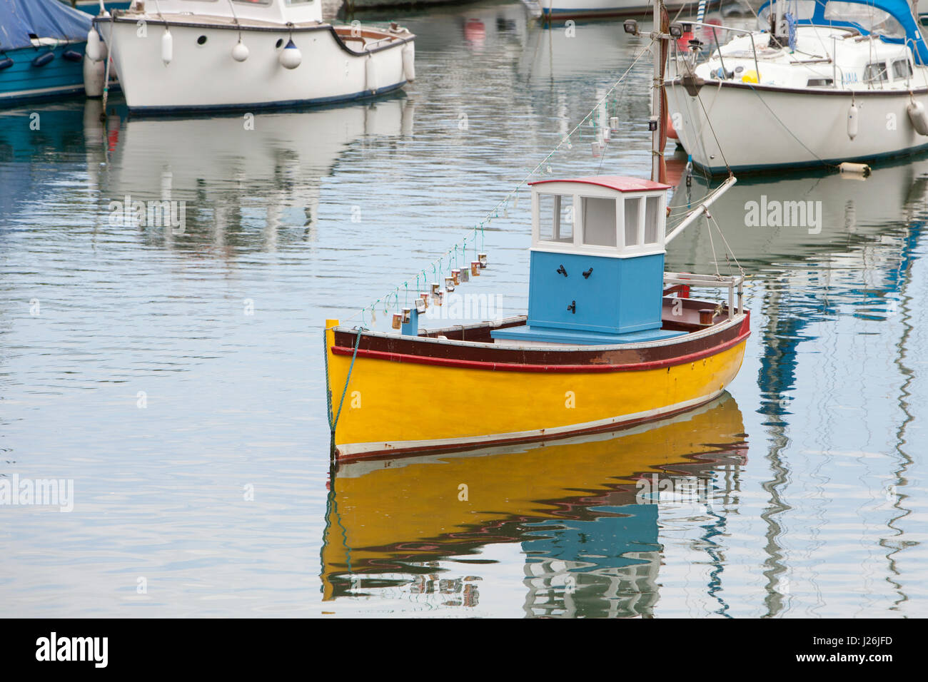Eine gelbe geschälten Boot mit einer blauen Kabine befindet sich im ruhigen Wasser des Porthleven Hafen, Cornwall, UK Stockfoto