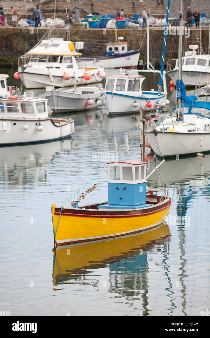Eine gelbe geschälten Boot mit einer blauen Kabine befindet sich im ruhigen Wasser des Porthleven Hafen, Cornwall, UK Stockfoto