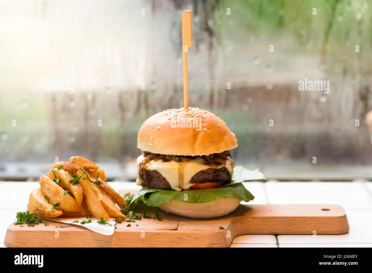 Hausgemachte Hamburger mit Rindfleisch, Salat, Käse, Tomaten und Kartoffeln Pommes Frites auf Tablett aus Holz. Stockfoto