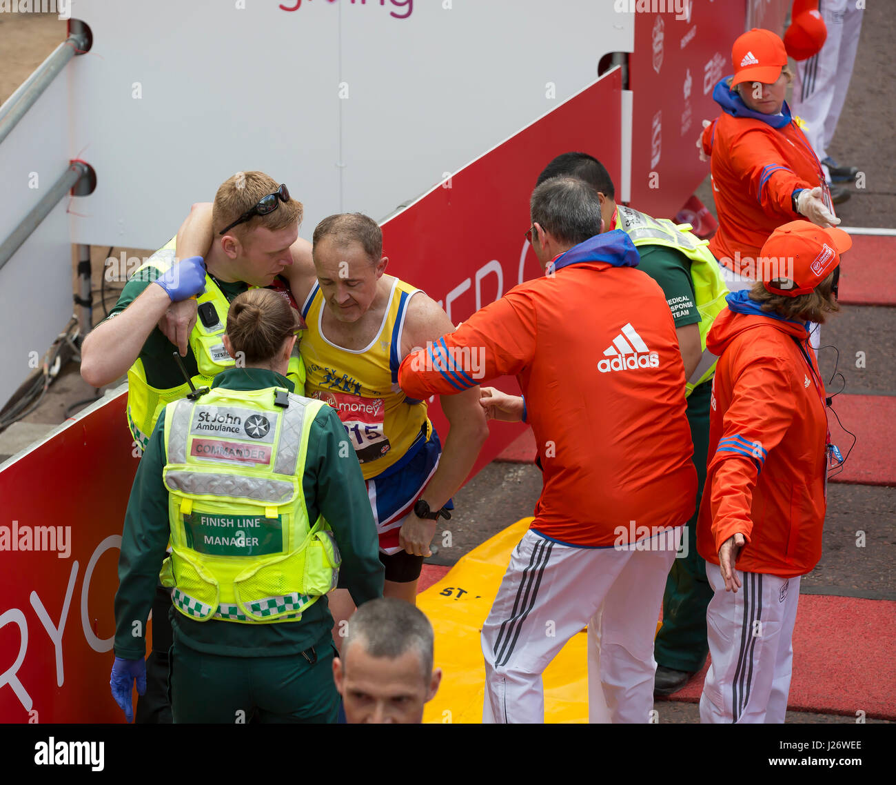 Ein Mann muss über die Linie Virgin London Marathon zu beenden, in der Mall geholfen werden Stockfoto