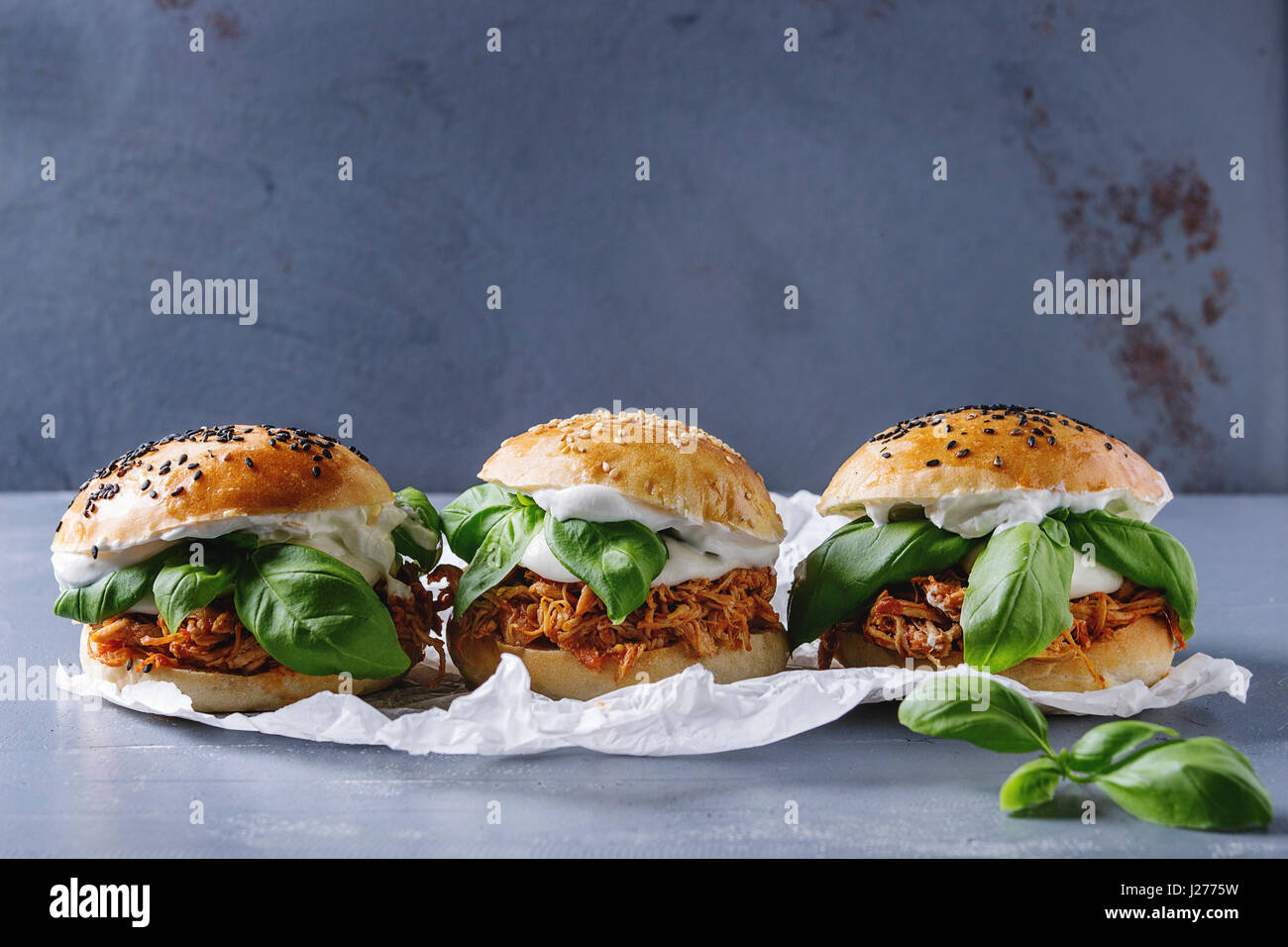Hausgemachte Mini-Burger mit gezogener Huhn, Basilikum, Mozzarella-Käse und Joghurt-Sauce auf Backpapier über graue Textur Hintergrund. Gesundes Fast Food c Stockfoto