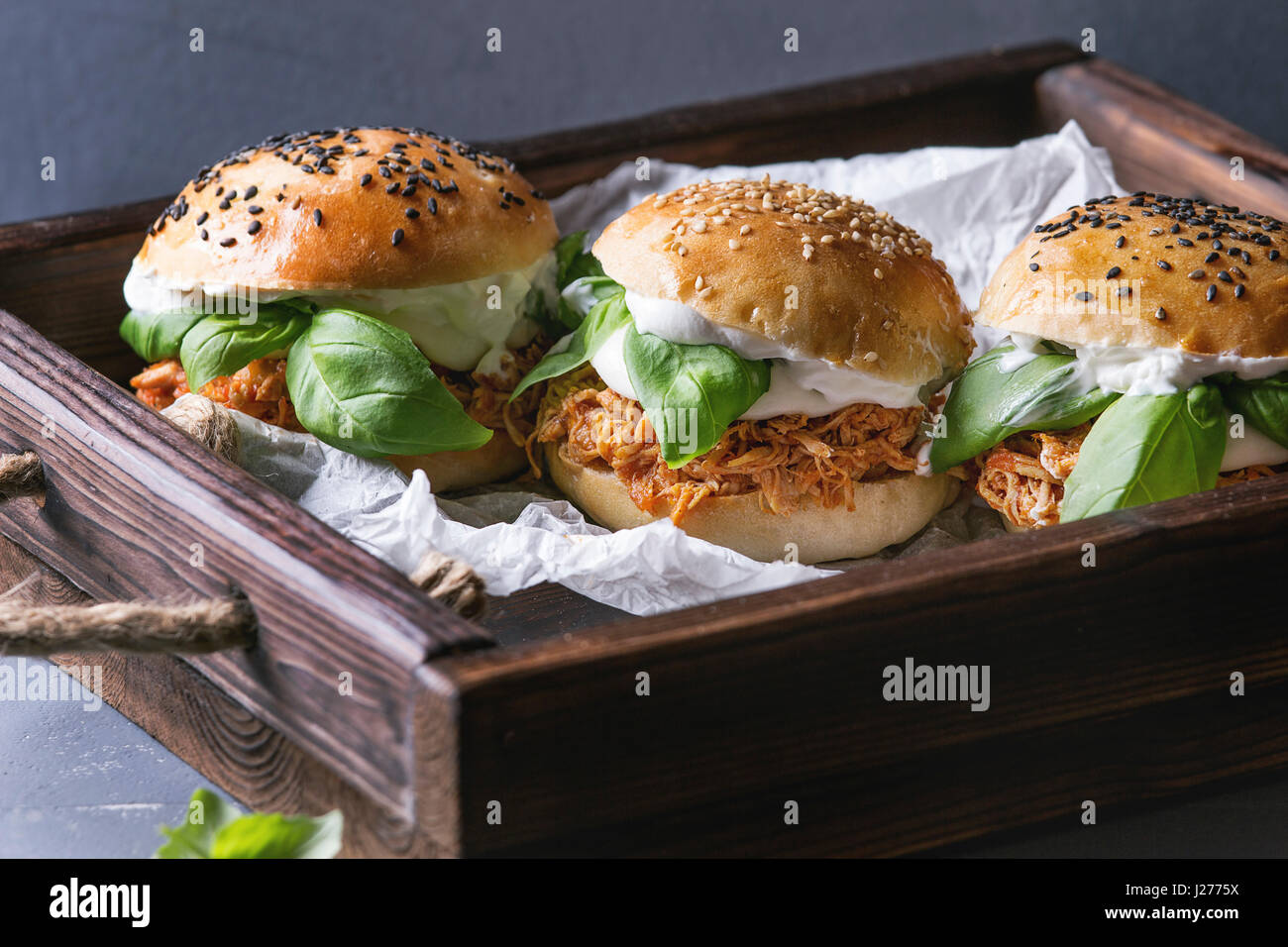 Hausgemachte Mini-Burger mit gezogener Huhn, Basilikum, Mozzarella-Käse und Joghurt-Sauce auf Holztablett mit Backpapier über graue Textur Hintergrund. Er Stockfoto