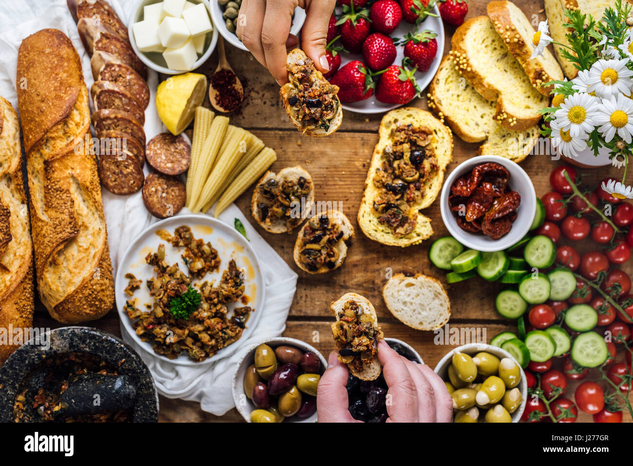 Ein Mann und eine Frau packte Brotscheiben mit Oliven Tapenade aus einem Holzbrett mit französischem Baguette, Wurst, Baby Hühneraugen, Käse, Strawberr e geladen Stockfoto